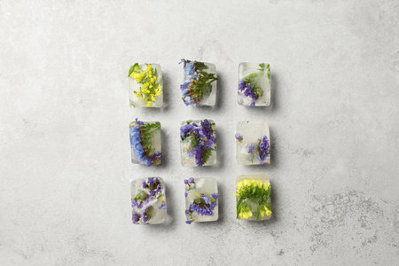 Ice cubes with flowers on light stone background, flat lay
