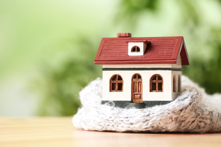 House model and scarf on wooden table against blurred background, space for text. heating efficiencyの写真素材