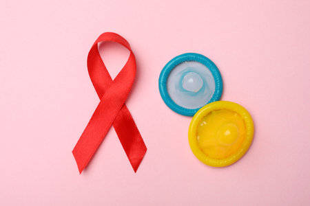 Flat lay composition with colorful condoms and red ribbon on pink background. LGBT conceptの写真素材