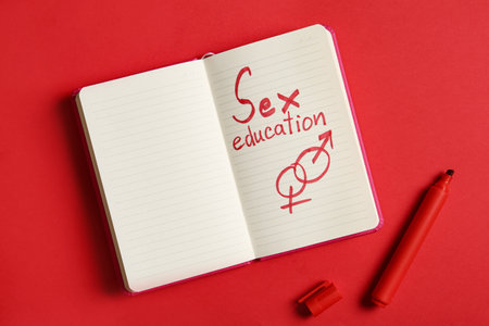 Notebook with phrase "SEX EDUCATION" on red background, flat lay. Space for textの写真素材