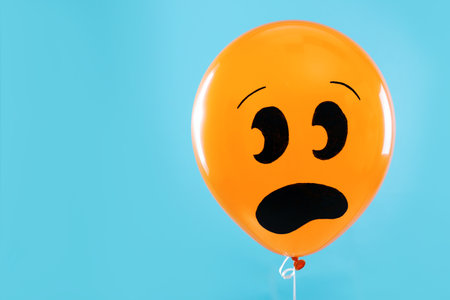 Orange balloon with drawing of scared face on blue background, space for text. halloween party