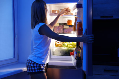 Woman taking products out of refrigerator in kitchen at nightの写真素材