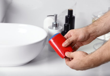 Man holding stick deodorant in bathroom, closeup view. Space for textの写真素材