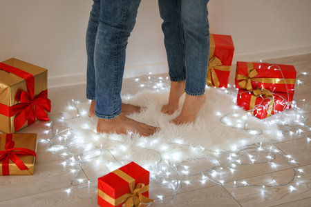 Young couple standing on rug near Christmas lights and gift boxes, closeupの写真素材