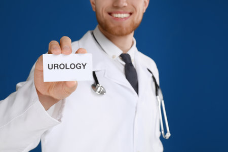 Male doctor holding card with word UROLOGY on blue background, closeupの写真素材