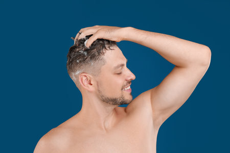 Handsome man washing hair on blue backgroundの写真素材