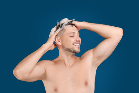 Handsome man washing hair on blue backgroundの写真素材