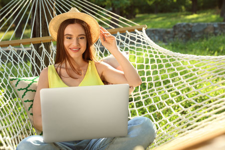Young woman with laptop resting in comfortable hammock at green gardenの写真素材