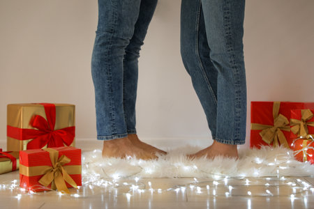 Young couple standing on rug near Christmas lights and gift boxes, closeupの写真素材