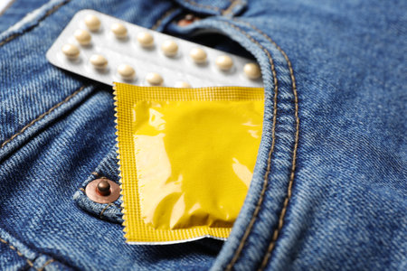 Yellow condom and birth control pills in pocket of jeans, closeup. safe sex conceptの写真素材