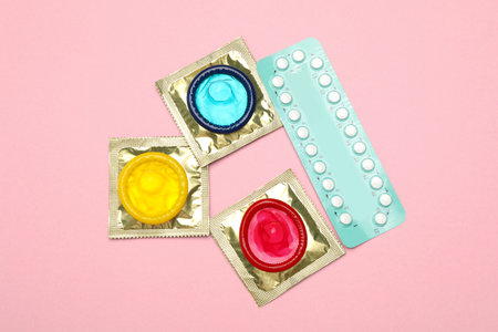 Condoms and birth control pills on pink background, top view. safe sexの写真素材
