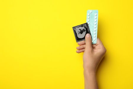 Woman holding condom and birth control pills on yellow background, top view with space for text. safe sexの写真素材