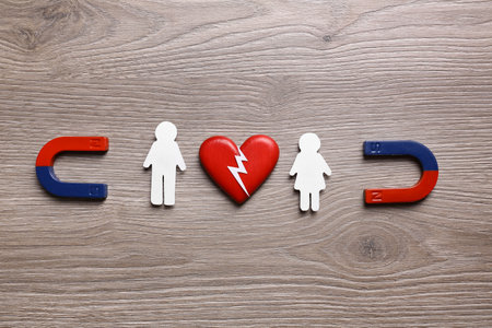 Magnets attracting paper couple on wooden background, flat lay. love concept