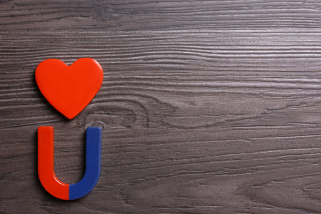 Red and blue horseshoe magnet with decorative heart on dark gray wooden background, flat lay. Space for textの写真素材