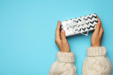Young woman holding Christmas gift on light blue background, top view. Space for textの写真素材