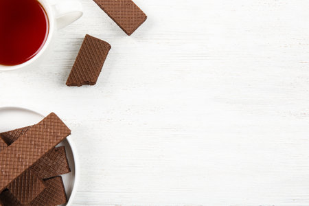 Plate of delicious chocolate wafers with cup of tea on white wooden background, top view. Space for textの写真素材