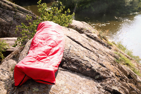 Man resting in sleeping bag on cliff near lakeの写真素材
