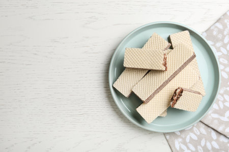 Plate of delicious crispy wafers with chocolate filling on white wooden table, top view. Space for textの写真素材