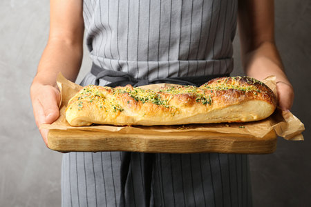 Woman holding tasty homemade garlic bread with cheese and herbs against gray backgroundの写真素材