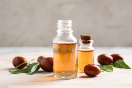 Glass bottles with jojoba oil and seeds on light table against gray backgroundの写真素材