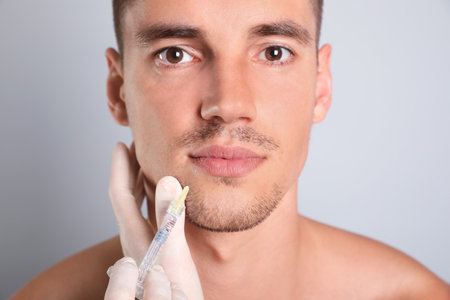 Man getting facial injection on gray background, closeup. cosmetic surgeryの写真素材