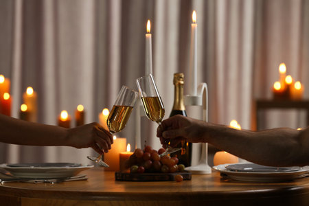 Couple clinking glasses of champagne at table with burning candles, closeupの写真素材