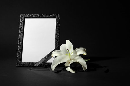 Funeral photo frame with ribbon and white lily on black background. space for designの写真素材