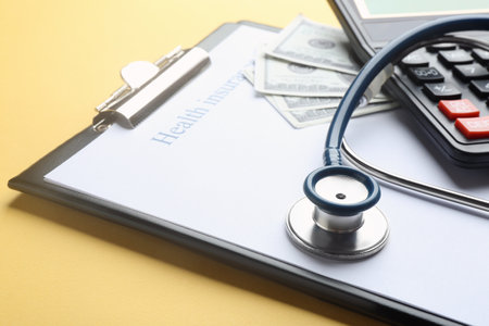 Clipboard with medical insurance form, money, calculator and stethoscope on yellow background, closeupの写真素材