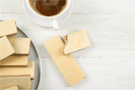 Plate of delicious wafers with cup of coffee on white wooden background, top view. Space for textの写真素材
