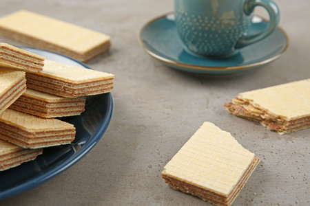 Plate of delicious wafers with cup of drink on gray stone background, closeup