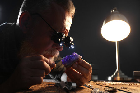 Male jeweler evaluating amethyst at table in workshopの写真素材
