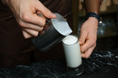 Barista pouring milk into glass cup for coffee drink at tableの写真素材