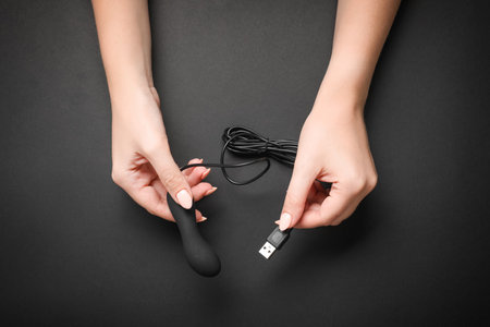 Young woman holding little vibrator with charging cable on black background, top view. sex toyの写真素材