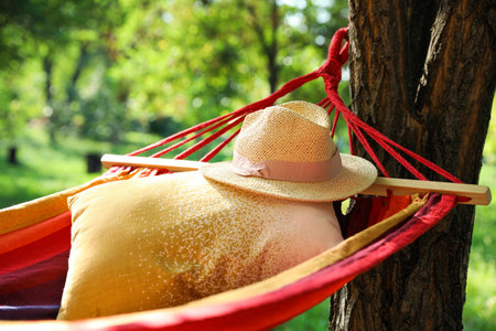 Bright comfortable hammock with pillow and hat hanging in green garden, closeupの写真素材