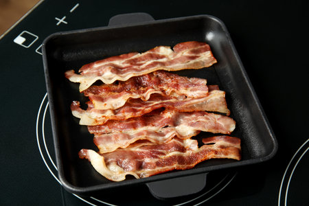 Slices of tasty fried bacon on kitchen stoveの写真素材