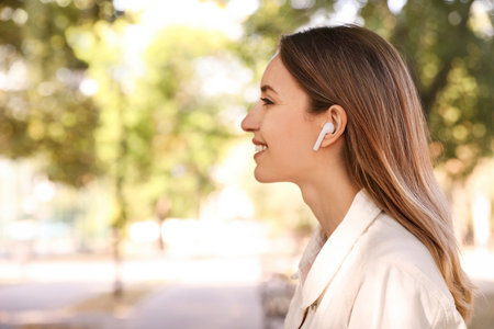 Young woman with wireless headphones listening to music in park. Space for textの写真素材