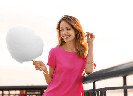 Happy young woman with cotton candy on waterfront