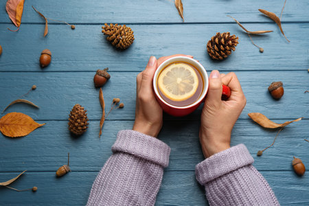 Woman with cup of hot drink at blue wooden table, top view. Cozy autumn atmosphereの写真素材