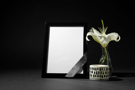 Funeral photo frame with ribbon, white lily and candle on black background. space for designの写真素材