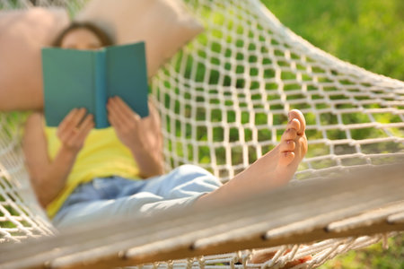 Young woman reading book in comfortable hammock at green gardenの写真素材