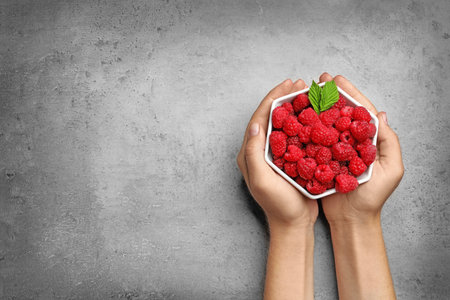 Woman holding bowl with delicious ripe raspberries on stone background, top view. Space for textの写真素材