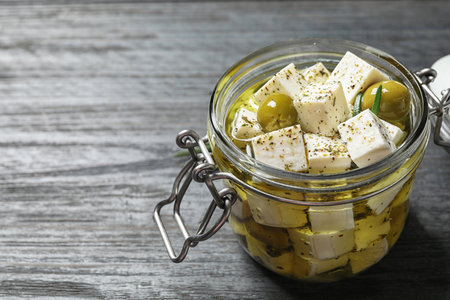 Pickled feta cheese in jar on gray wooden table, space for text