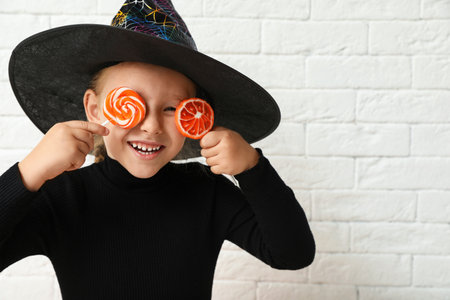 Cute little girl with candies wearing Halloween costume near white brick wall. Space for textの写真素材