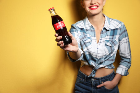 MYKOLAIV, UKRAINE - NOVEMBER 28, 2018: Young woman with bottle of Coca-Cola on color background,...