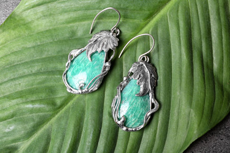Beautiful pair of silver earrings with amazonite gemstones on green leaf, above viewの写真素材