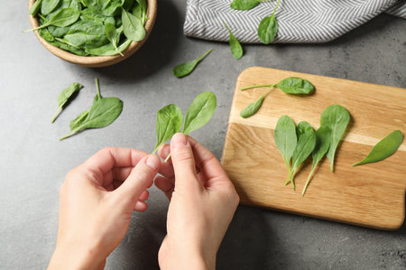 Woman with fresh green healthy spinach at gray table, top view