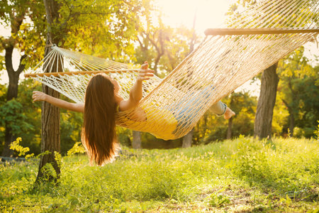 Young woman resting in comfortable hammock at green gardenの写真素材