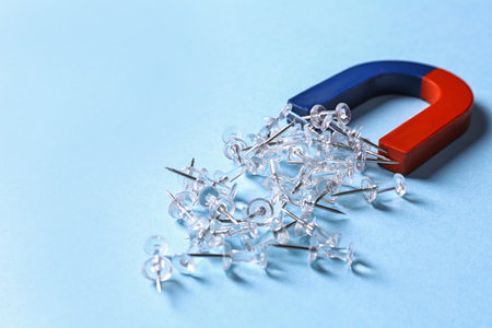 Red and blue horseshoe magnet attracting push pins on light blue backgroundの写真素材