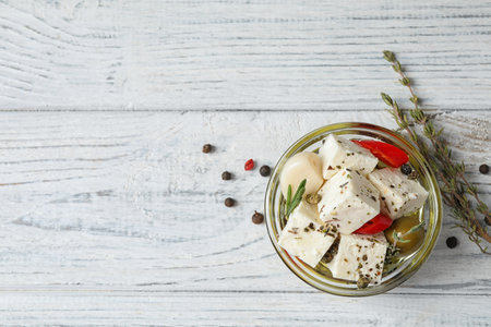 Pickled feta cheese in bowl on white wooden table, top view. Space for textの写真素材