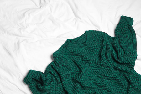 Dark green knitted sweater on white fabric, flat lay. Space for textの写真素材